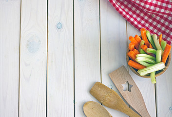 Culinary background. The white wooden surface on it is a red kitchen towel in a cage, vegetables and wooden spatulas for cooking