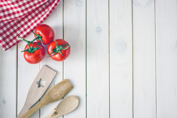 Culinary background. The white wooden surface on it is a red kitchen towel in a cage, vegetables and wooden spatulas for cooking