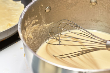 Fototapeta na wymiar Whisk in pan with batter for pancakes, close-up