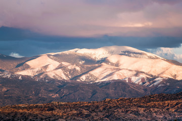 Fototapeta na wymiar Sunset illuminates the snow-capped Sangre de Cristo Mountains and colorful clouds and badlands near Santa Fe, New Mexico