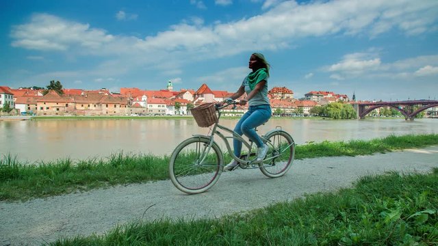 Cycling down the path on the riverside. It's a nice summer day and we can see a beautiful city of Maribor on the other side of the river.