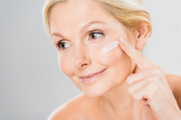 beautiful and mature woman looking away and applying cosmetic cream on face