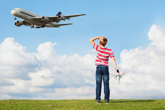Boy holding model plane while passenger plane flies overhead