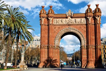 Fototapeta na wymiar Triumphal Arch in Barcelona, Catalonia, Spain. Arc de Triomf at boulevard street. Alley with tropical palm trees. Early morning landscape with shadows and blue sky with clouds. Famous landmark.