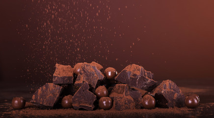 Arrangement of pieces of chocolate and round candies sprinkled with cocoa powder on brown