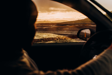 The driver rides behind the wheel and looks at the sunset. Silhouette of the driver in the car at sunset.
