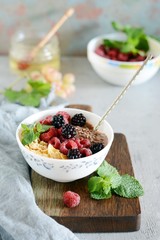 Sunday Breakfast. Oatmeal porridge with banana and flax seed, raspberries, blackberries, corn flakes, honey and mint, selective focus. Useful food, diet. Plate or cup with vegan porridge, smoothies 