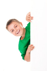 Emotional positive smiling boy in bright green t-shirt and posing behind a white panel isolated on white background. Place for banner advertising