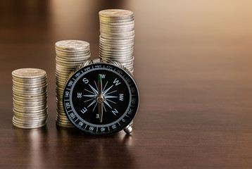 Stack of coins with compass on wood table
