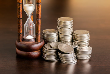 Stack of coins with hourglass on wood table