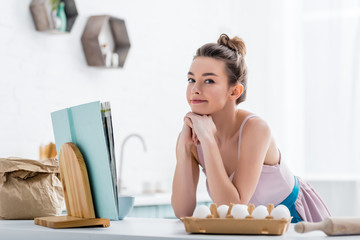 happy attractive girl near cookbook and eggs looking at camera