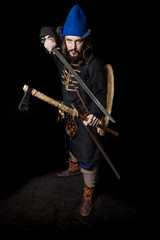 Fototapeta premium a man in clothes and with weapons of the Viking Age threatens with a sword and ax