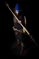 a man in clothes and with weapons of the Viking Age threatens with a spear