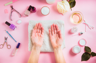 Top view opened female hands on the white towel surounded cosmetics and accessories for manicure and skin care. Flat lay composition on pink background for beauty blog.