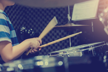 blurry image of wooden drumsticks in hands of Asian kid wearing blue striped t-shirts to learning...