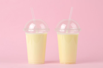 Making a milkshake. plastic disposable glass with a banana milkshake on a bright trendy pink background.