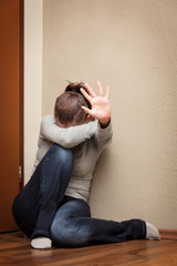 Frau sitzt in der Ecke, Hand zum Schutz nach oben gestreckt, häusliche Gewalt