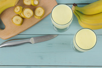 A glass with a banana milkshake and a fresh banana on a wooden blue table. Making a milkshake. top view