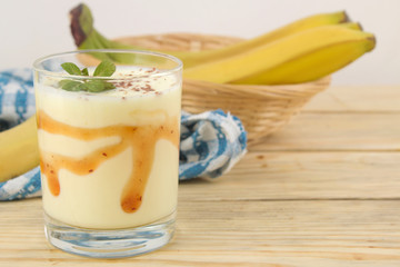 a glass with a banana milkshake, syrup and chocolate chips and a fresh banana on a natural wooden table. Making a milkshake.