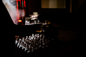 man holding a drink glass while a waiter helps him, backlight with black background.