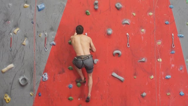 Free ambitious young man climbing on artificial wall. Guy reaching the top of mountain, slow motion