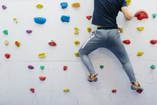 Strong and muscular sport climber exercising in the gym at artificial wall painted in white color