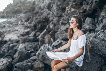 Pretty long hair tourist girl relaxing on the stones near sea.