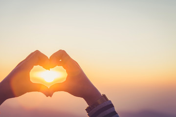 Hands forming a heart shape with sunrise silhouette,copy space,warm retro tone.
