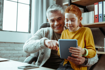 Joyful good looking man showing the tablet to his daughter
