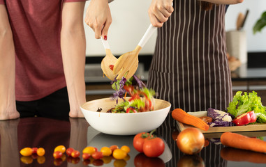 Asian young couple is feeding each other and smiling while cooking salad in kitchen