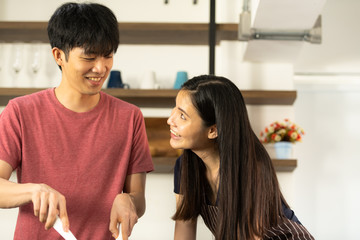 Asian young couple is feeding each other and smiling while cooking salad in kitchen