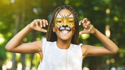 Cheerful little african-american girl with face painting like tiger