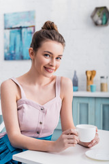 happy beautiful young woman sitting at table and drinking coffee