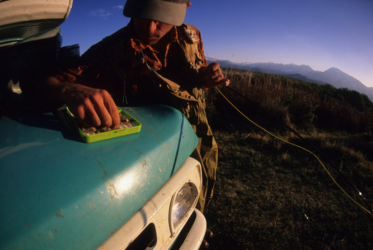 Fisherman Blake Treadway picks a fly from his green fly box while fly fishing in Bishop California.