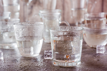 Many glasses of water splashed with drops and pieces of ice on a gray background
