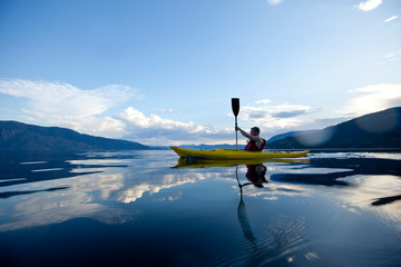 Young man paddles yellow kayak on Lake Pend Oreille in Sandpoint, Idaho.