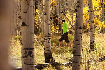 A young man walks a slackline through a gold aspen forest.