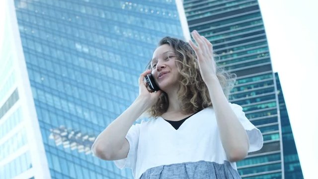 Young beautiful girl talking on the phone on the background of large glass skyscrapers