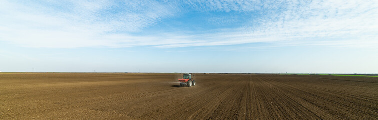 Obraz premium Ciągnik rozsiewający nawozy sztuczne na polu