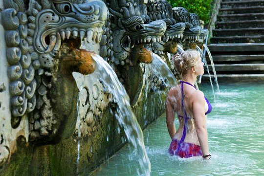 A beautiful woman relaxing in a hot springs surrounded by a lush jungle and flowers in Lovina, Bali, Indonesia.