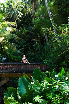 A beautiful woman relaxing on a bridge next to a hot springs surrounded by a lush jungle and flowers in Lovina, Bali, Indonesia.