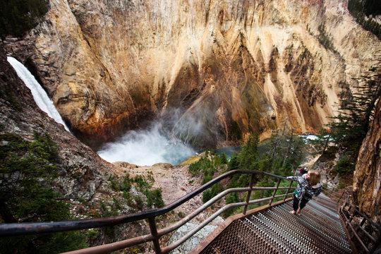 A young woman walks up a narrow stair set winds down to a overlook of Yellowstone Falls in Yellowstone National Park, Wyoming.