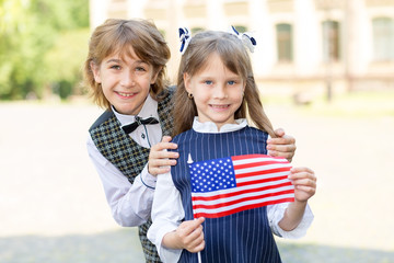 Schoolchildren boy and girl with the flag of the United States of America in their hands against...