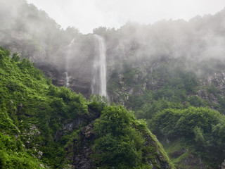 A powerful mountain stream flows down from the rocks in a dense fog.