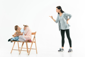 Obraz premium Angry mother scolding her son and daughter at home. Studio shot of emotional family. Human emotions, childhood, problems, conflict, domestic life, relationship concept