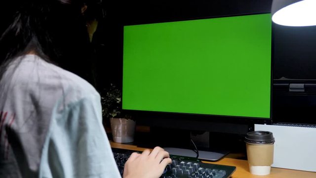 Dolly shot Asian girl sitting at her desk with Chroma key green screen background of computer monitor, Working at night