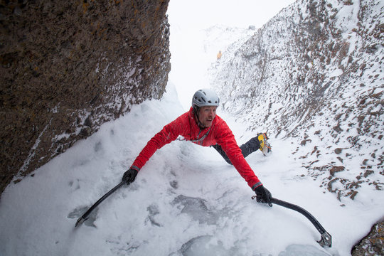 Zach Fletcher lead climbing water ice in wintery conditions while Todd Offenbacher belays below at Red Cliffs in Kirkwood, California.