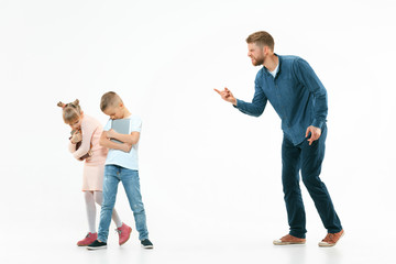 Naklejka premium Angry father scolding his son and daughter at home. Studio shot of emotional family. Human emotions, childhood, problems, conflict, domestic life, relationship concept