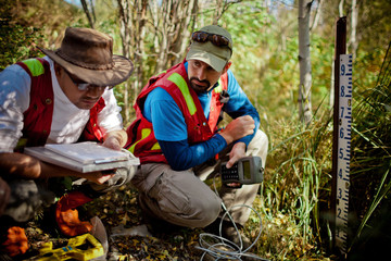 Two scientist collect data at a stream gauge in the field.