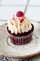 Homemade bakery style red velvet delicious sponge cupcake with white butter cream frosting and on raspberrie top on plate. Candy bar for celebrating partys and birthdays